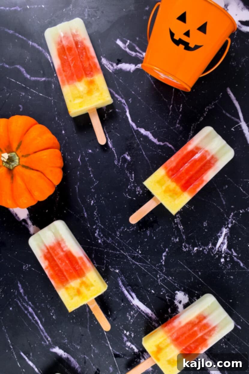 Vibrant melon, papaya, and pineapple popsicles resembling candy corn, garnished with a mini pumpkin and candle for a festive touch.