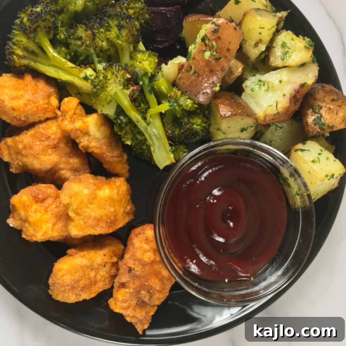 Popcorn chicken served with BBQ sauce, potatoes, and broccoli.