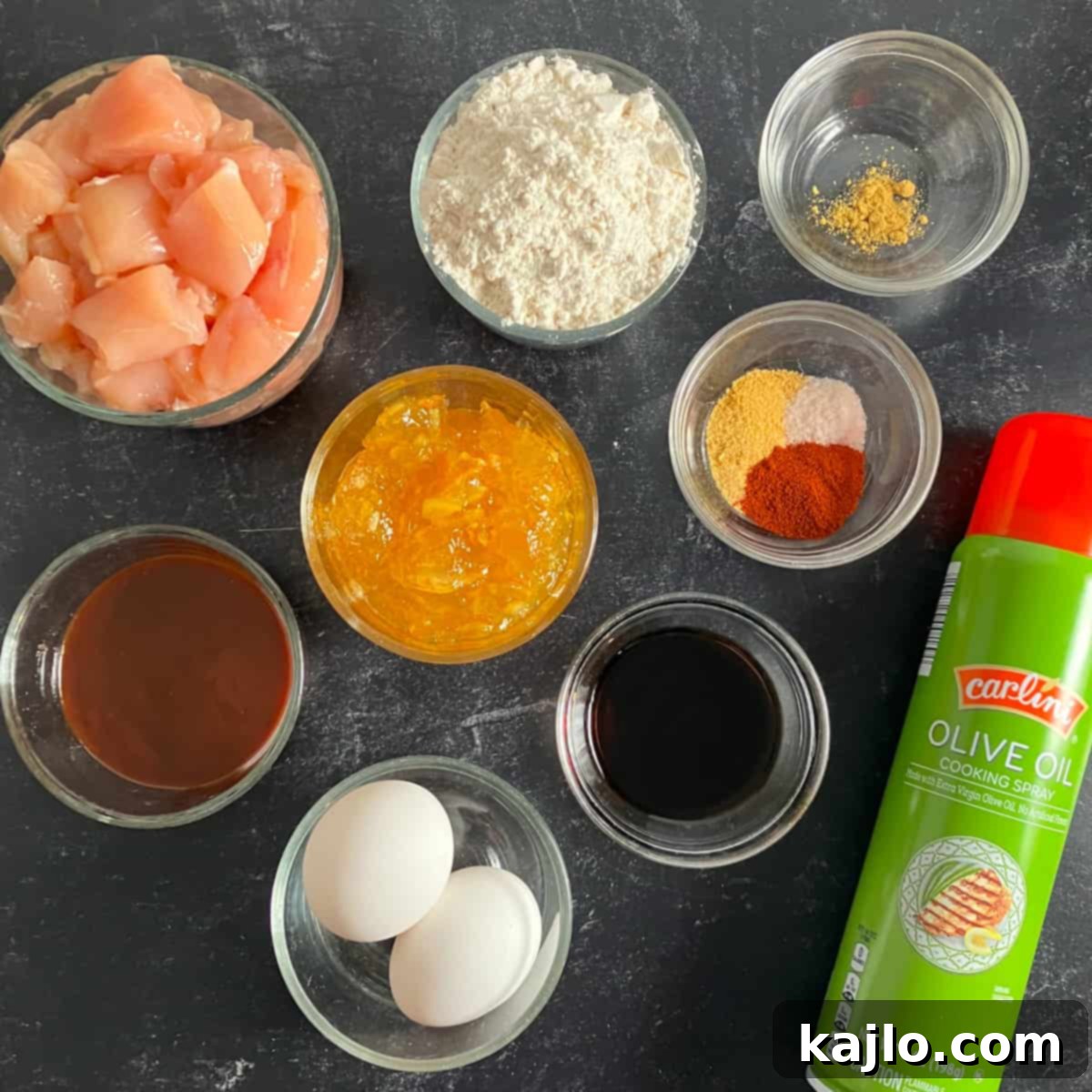 Ingredients laid out for making air fryer orange chicken, including chicken breast, flour, eggs, orange marmalade, and spices