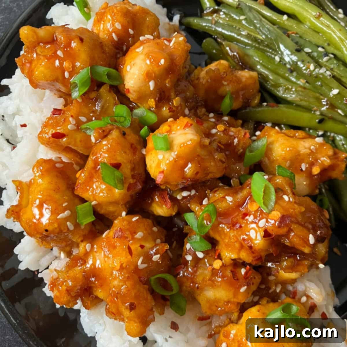 Plated Air Fryer Orange Chicken with orange marmalade sauce, garnished with sesame seeds and green onions, served over rice