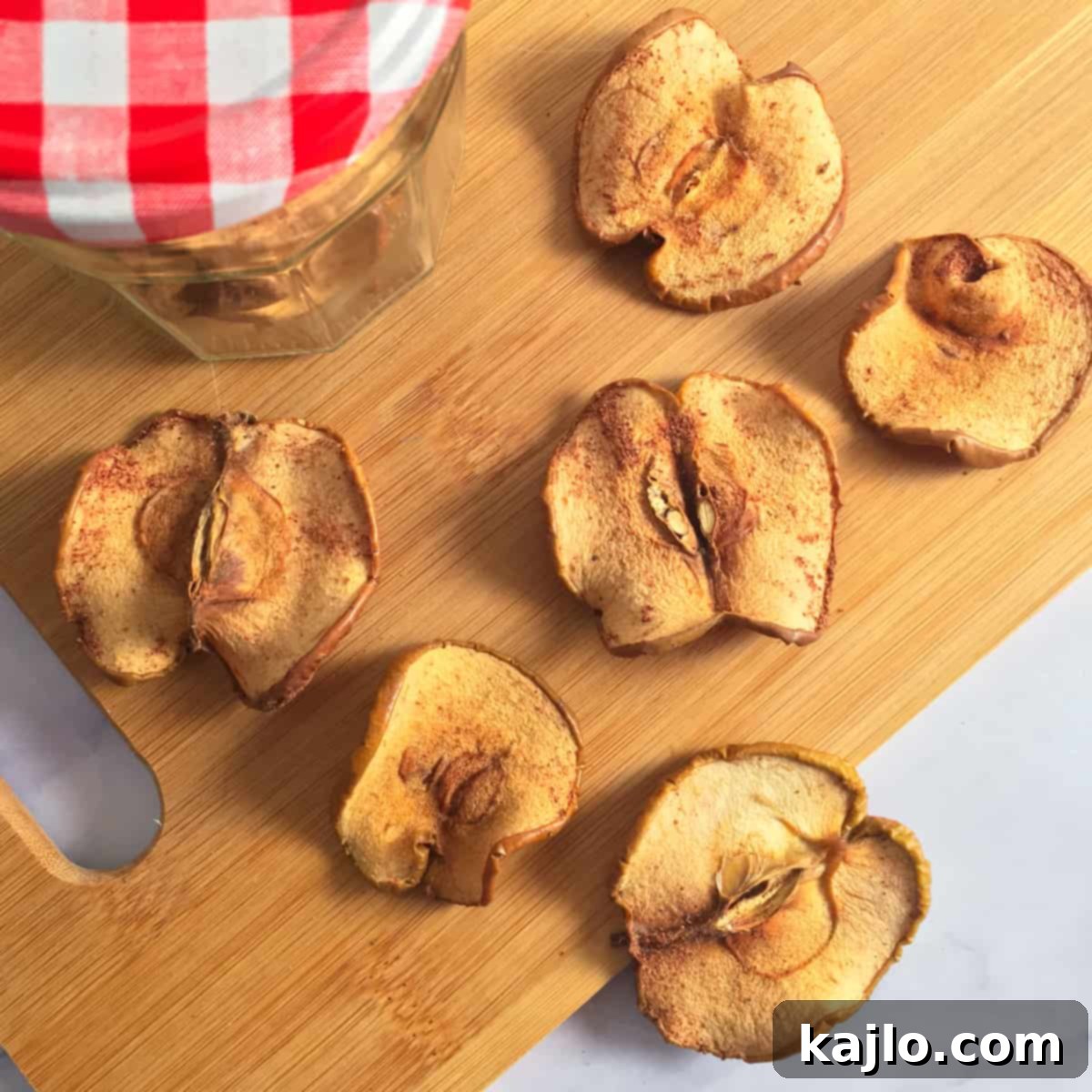 Crispy, golden-brown dehydrated cinnamon apple chips arranged artfully on a white surface, showcasing their natural sweetness and appealing texture.