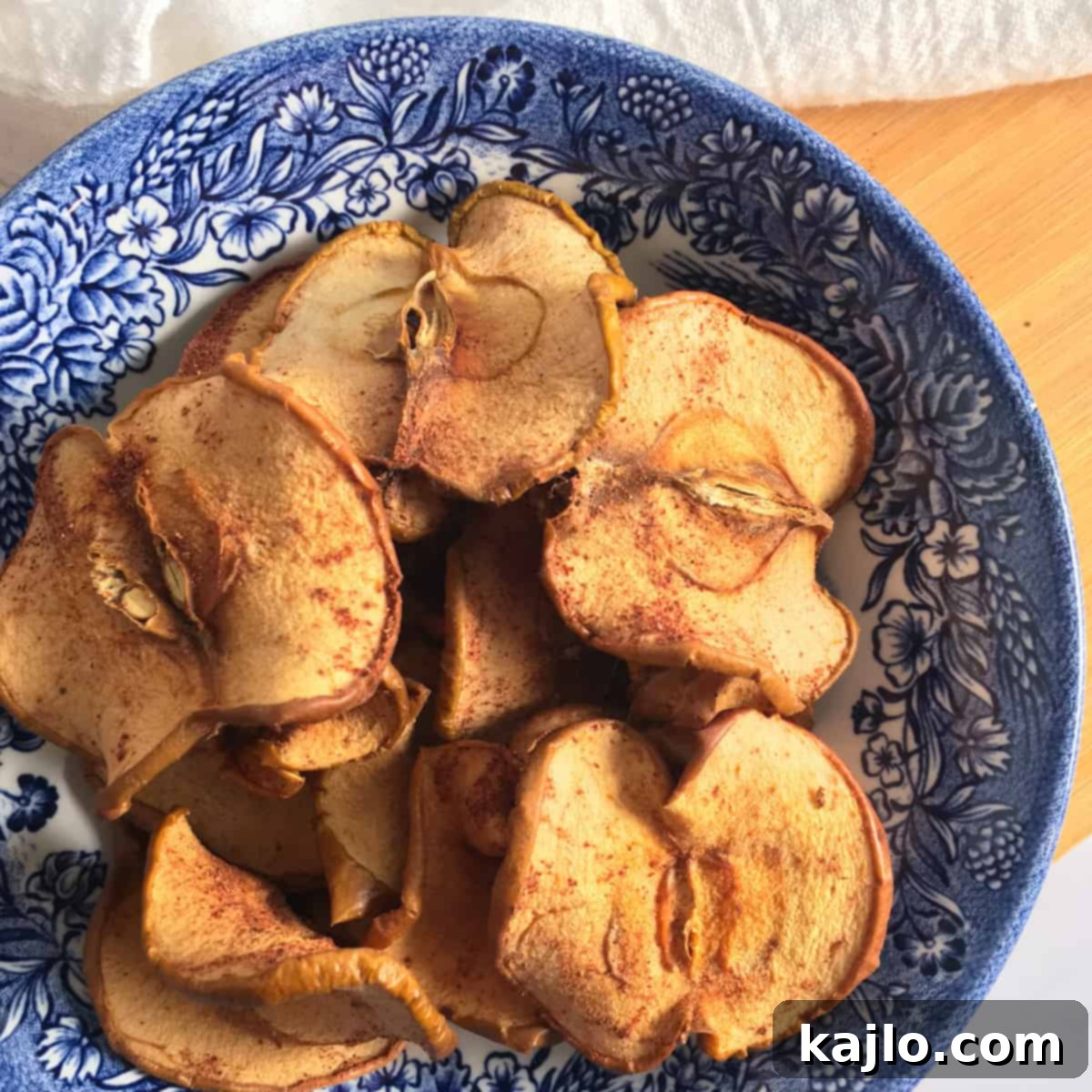 Thinly sliced dehydrated cinnamon apple slices, perfectly golden and slightly curled at the edges, on a baking sheet.