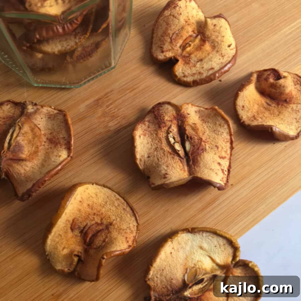 Close-up of crispy, thin dehydrated cinnamon apple slices on a baking tray, showing their texture and golden color.