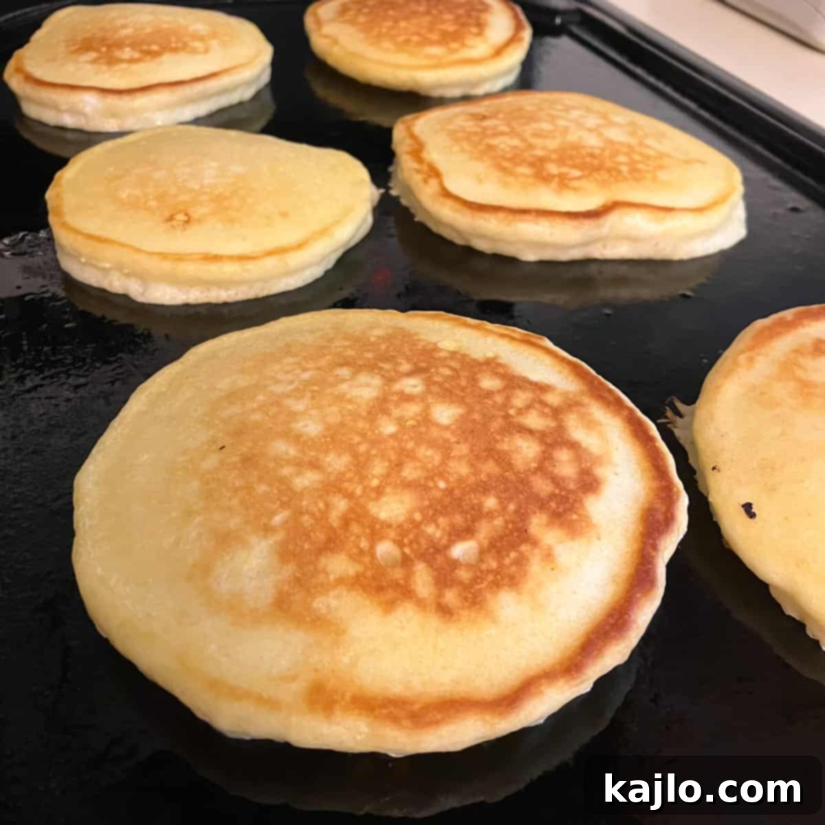 Pancake batter cooking on a griddle, forming golden-brown Denny's style pancakes.