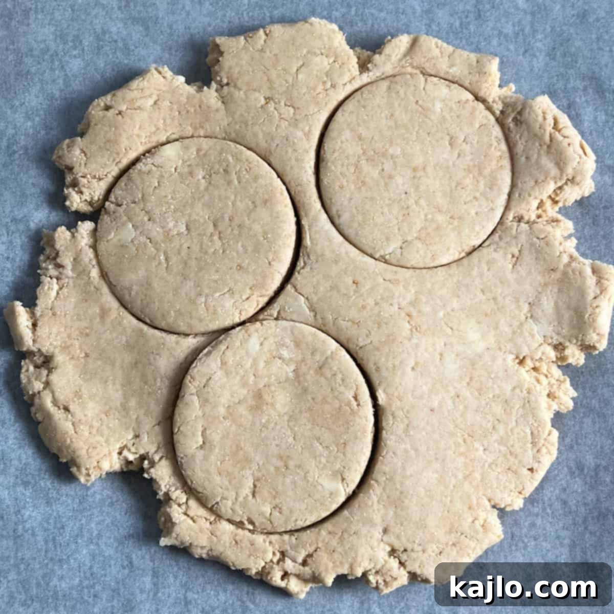 Kodiak protein biscuit dough being rolled out between parchment paper.